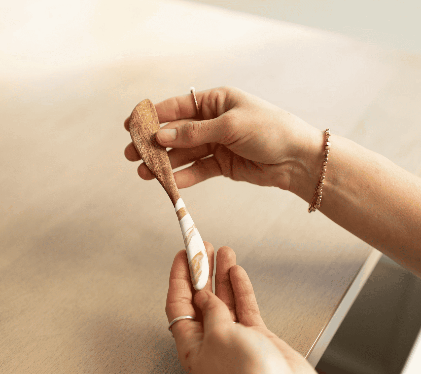 Hand holding a Lynn & Liana acacia wood cheese spreader with a white and gold Gold Quartz resin handle