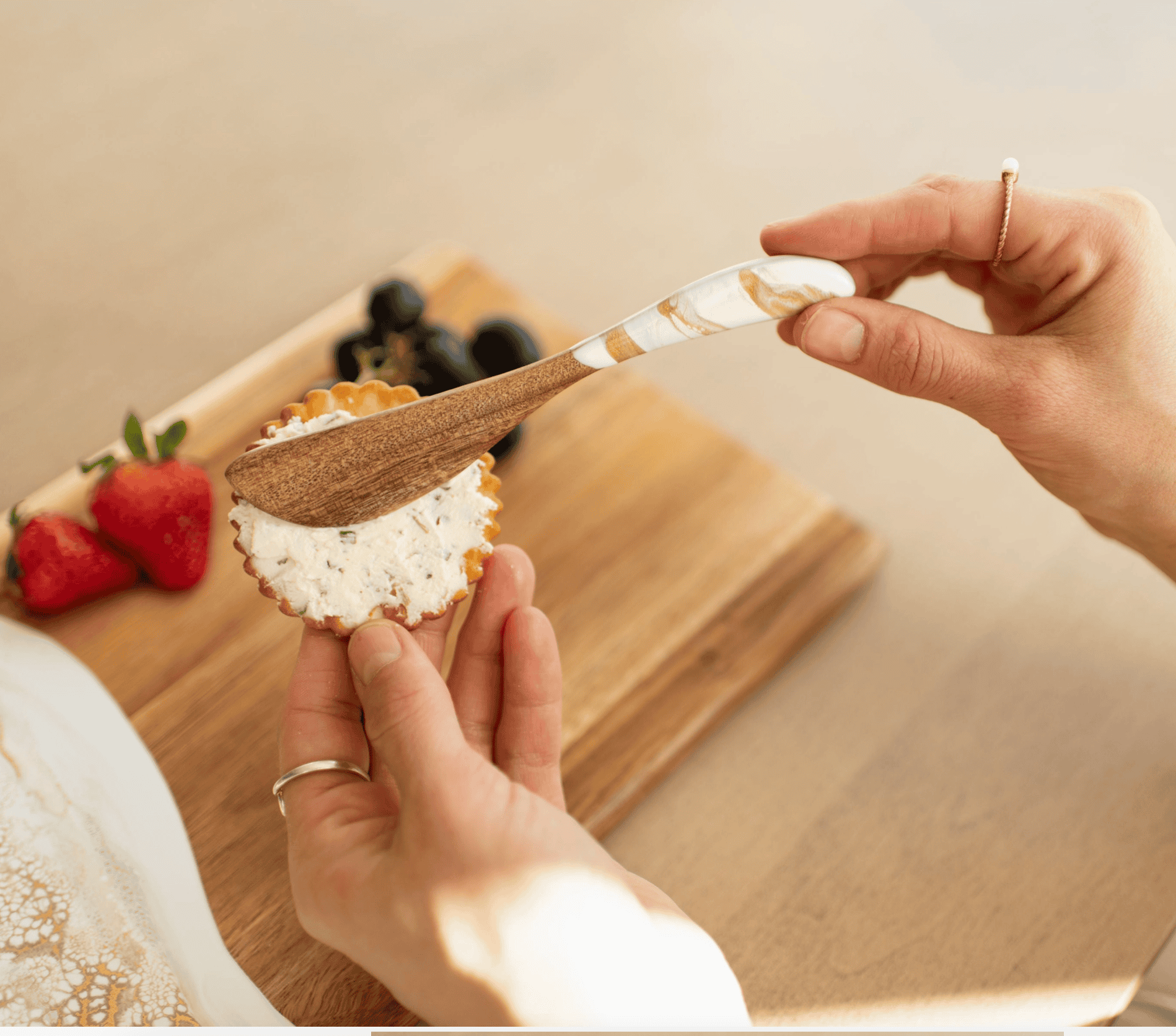 White and gold Gold Quartz acacia cheese spreader spreading soft cheese onto a cracker on a charcuterie board