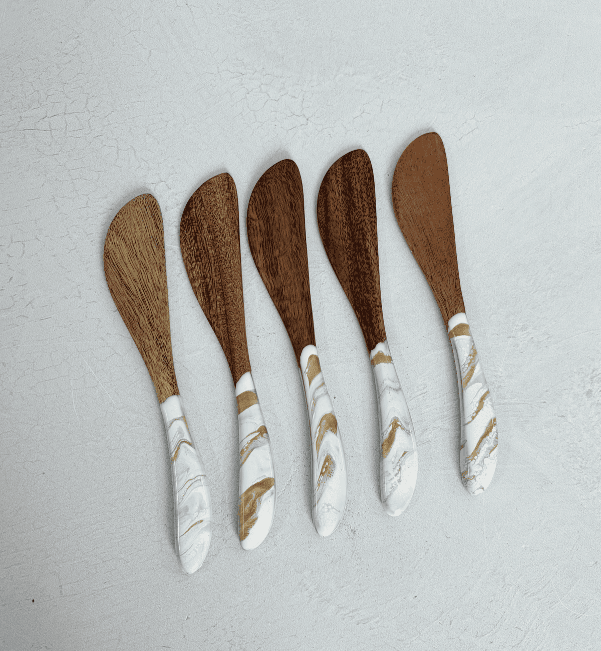 Set of five Lynn & Liana acacia cheese spreaders with white and gold Gold Quartz resin handles arranged in a row