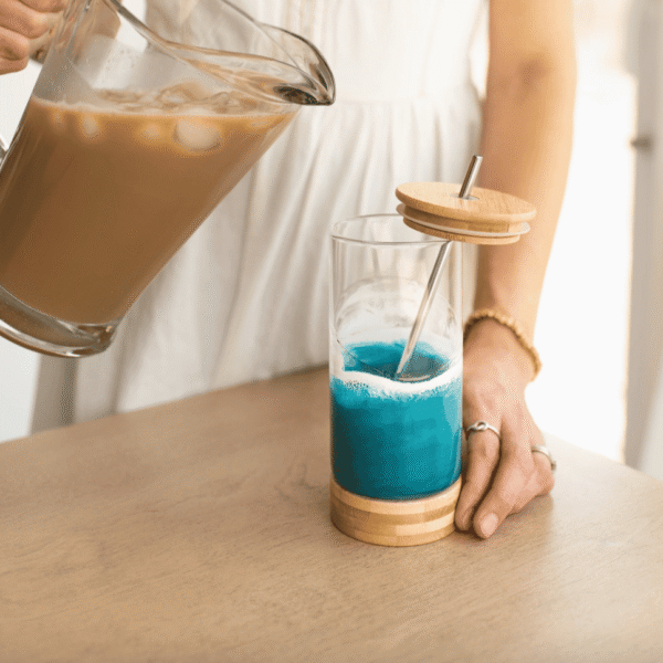 Ocean Vibes resin glass tumbler by Lynn & Liana with bamboo base and metal straw, being filled with iced coffee