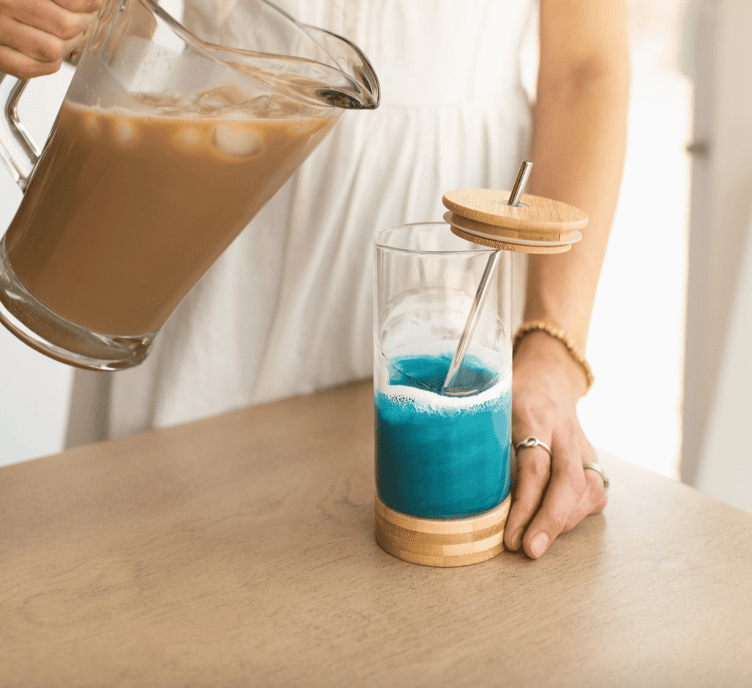 Ocean Vibes resin glass tumbler by Lynn & Liana with bamboo base and metal straw, being filled with iced coffee