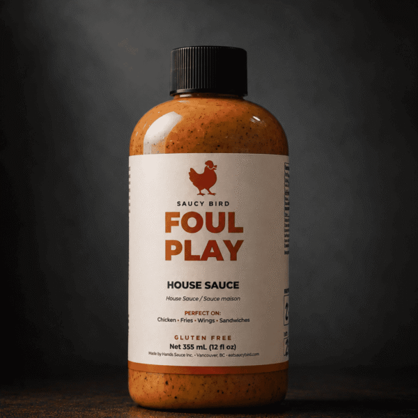 Bottle of Saucy Bird Foul Play House Sauce, a creamy gluten-free chicken sauce, 355 mL, on a dark background