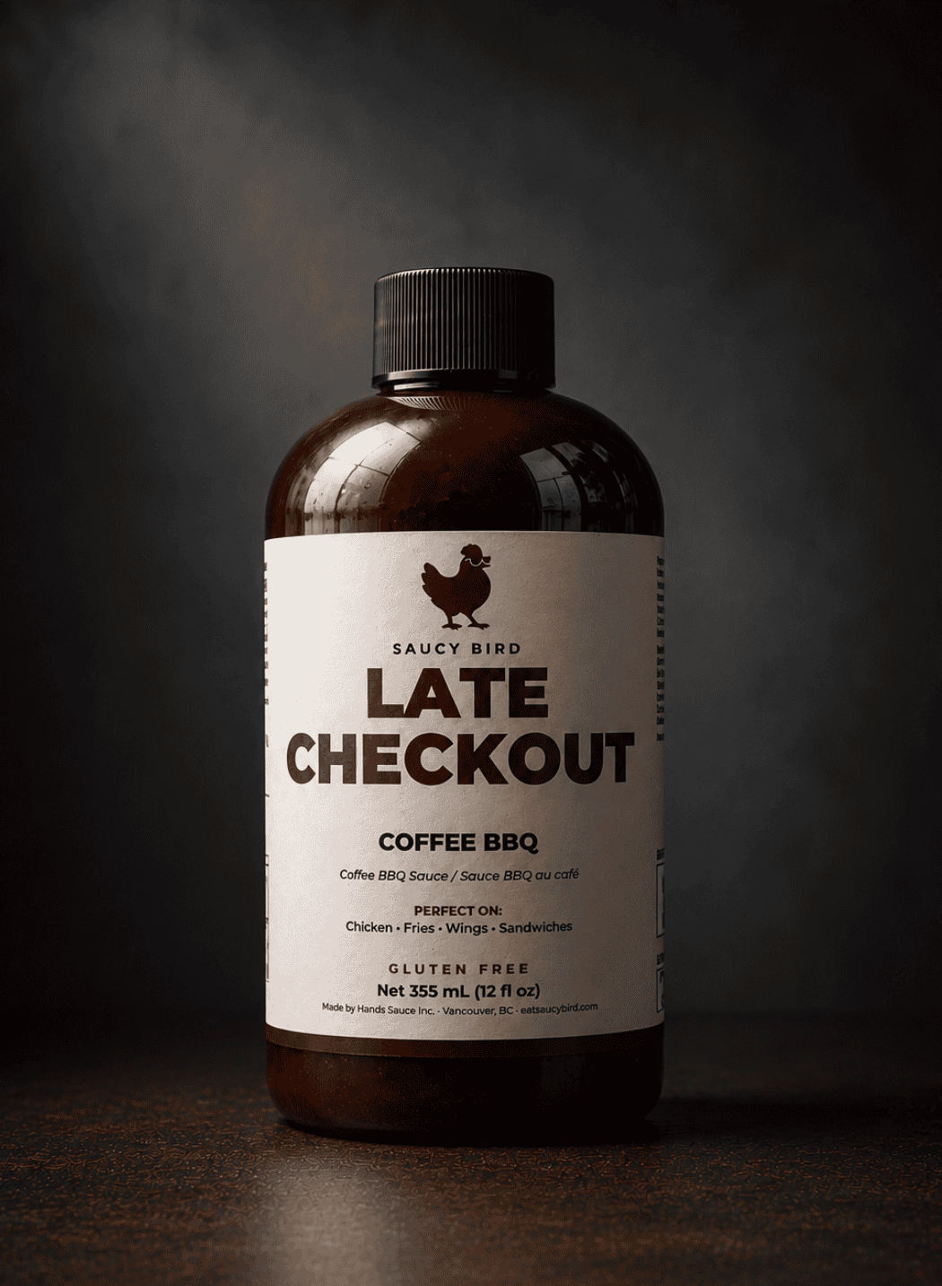 Bottle of Saucy Bird Late Checkout Coffee BBQ Sauce, 355 mL, on a dark grey background