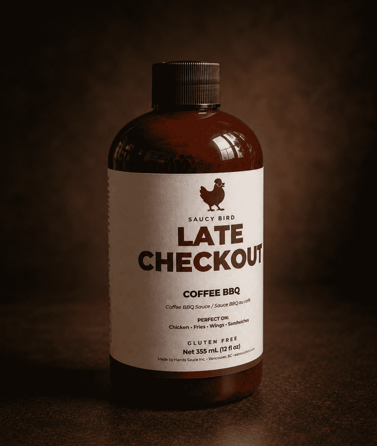 Bottle of Saucy Bird Late Checkout Coffee BBQ Sauce, 355 mL, on a warm dark background