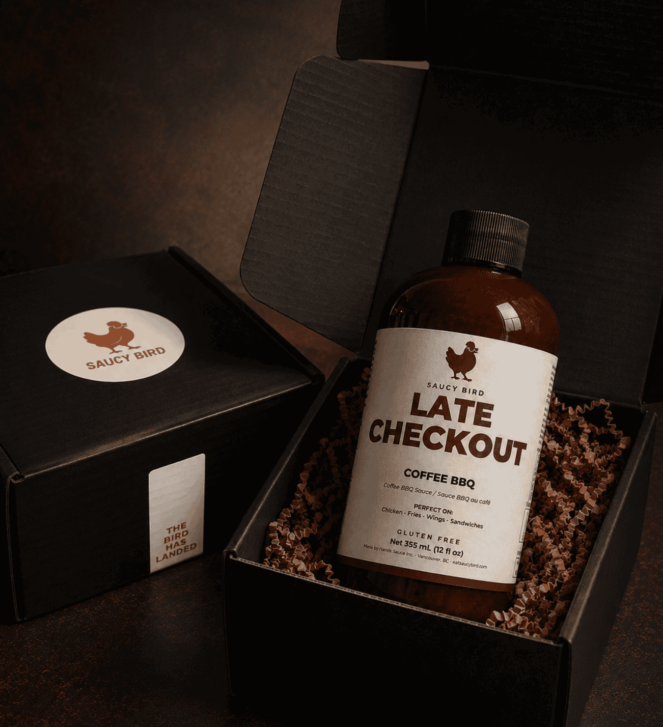 Bottle of Saucy Bird Late Checkout Coffee BBQ Sauce in an open black Saucy Bird gift box