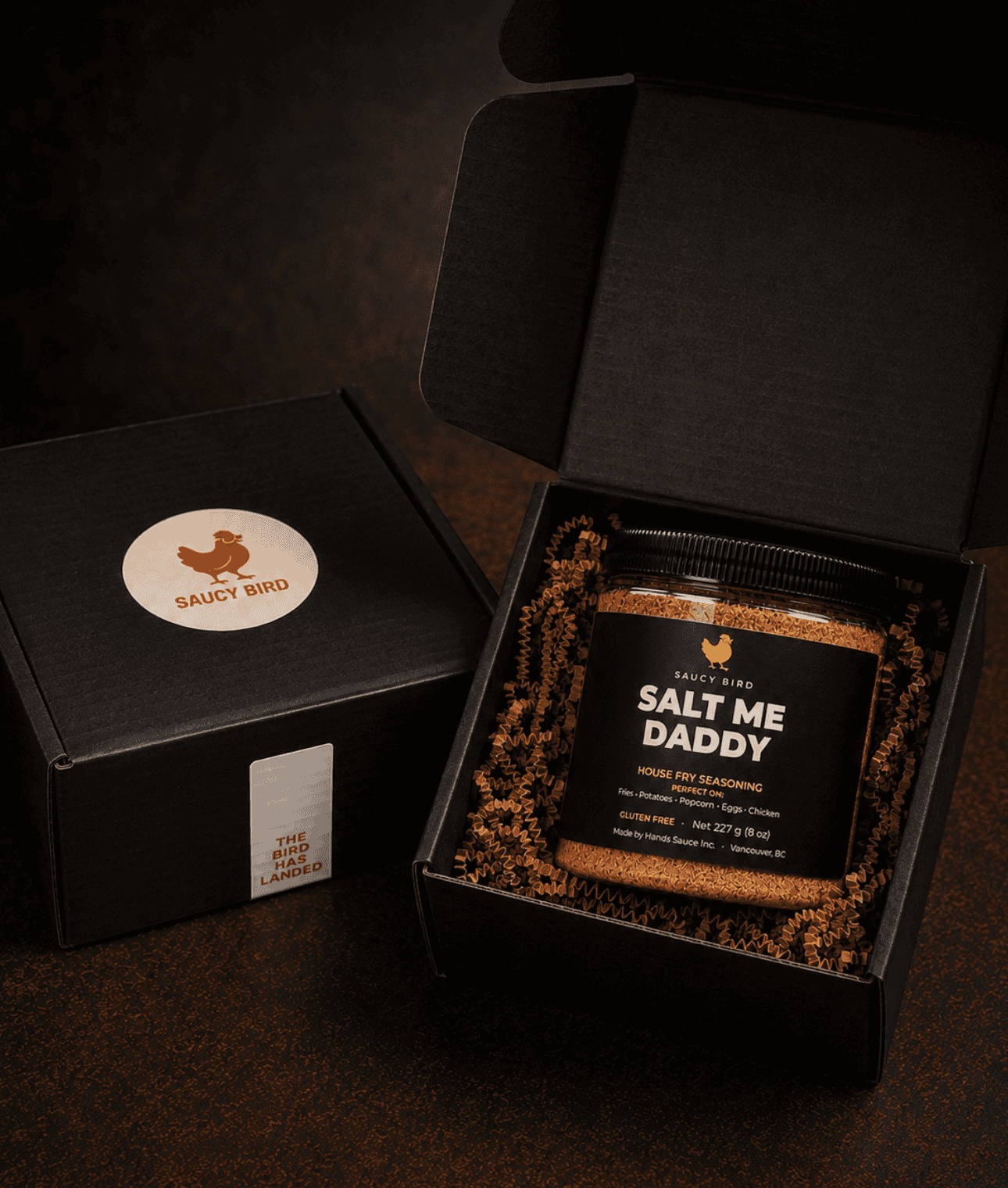 Jar of Saucy Bird Salt Me Daddy seasoning in an open black Saucy Bird gift box