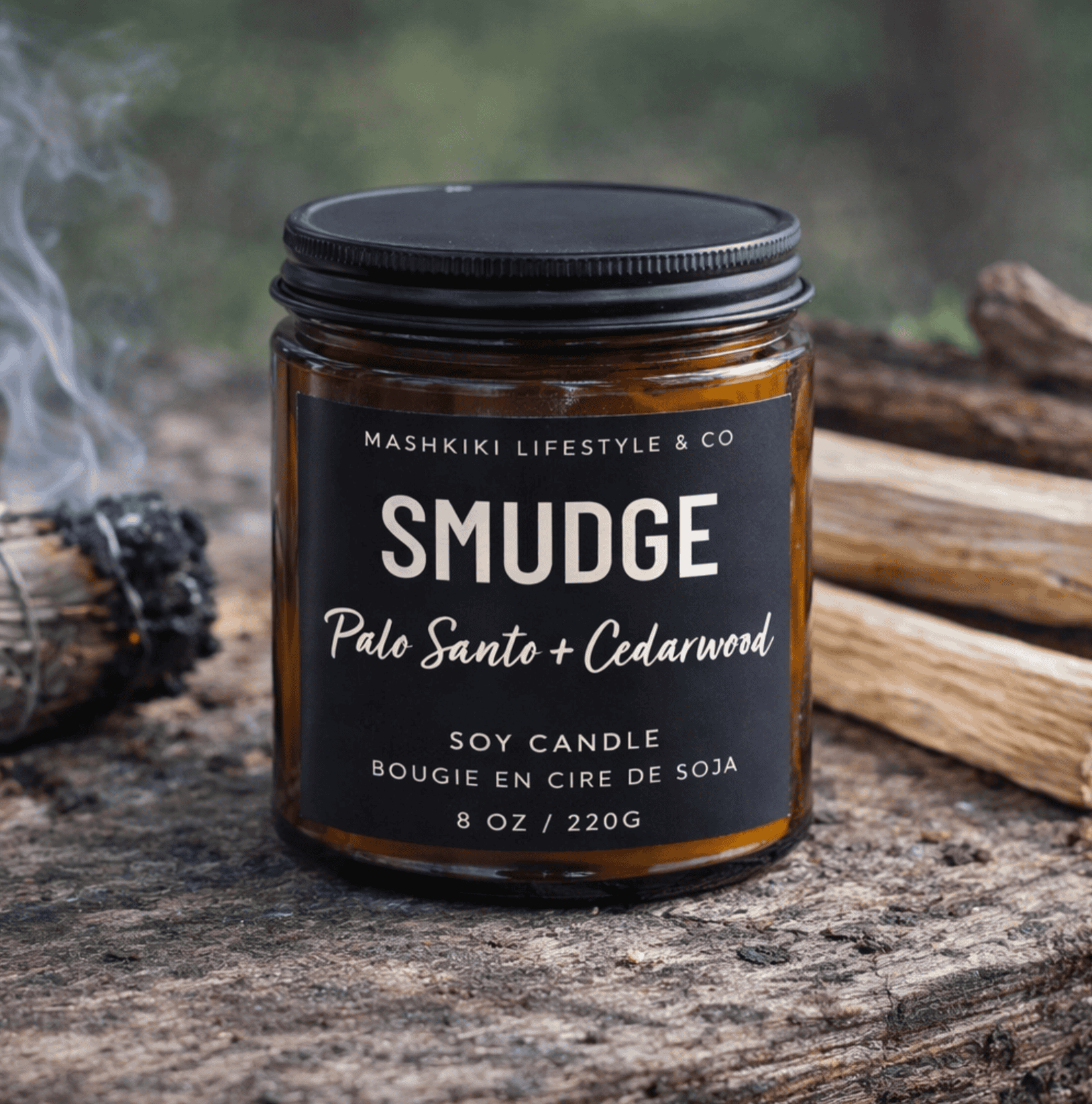Mashkiki Smudge 8 oz amber glass soy candle in Palo Santo + Cedarwood with a matte black lid, beside a smudge bundle
