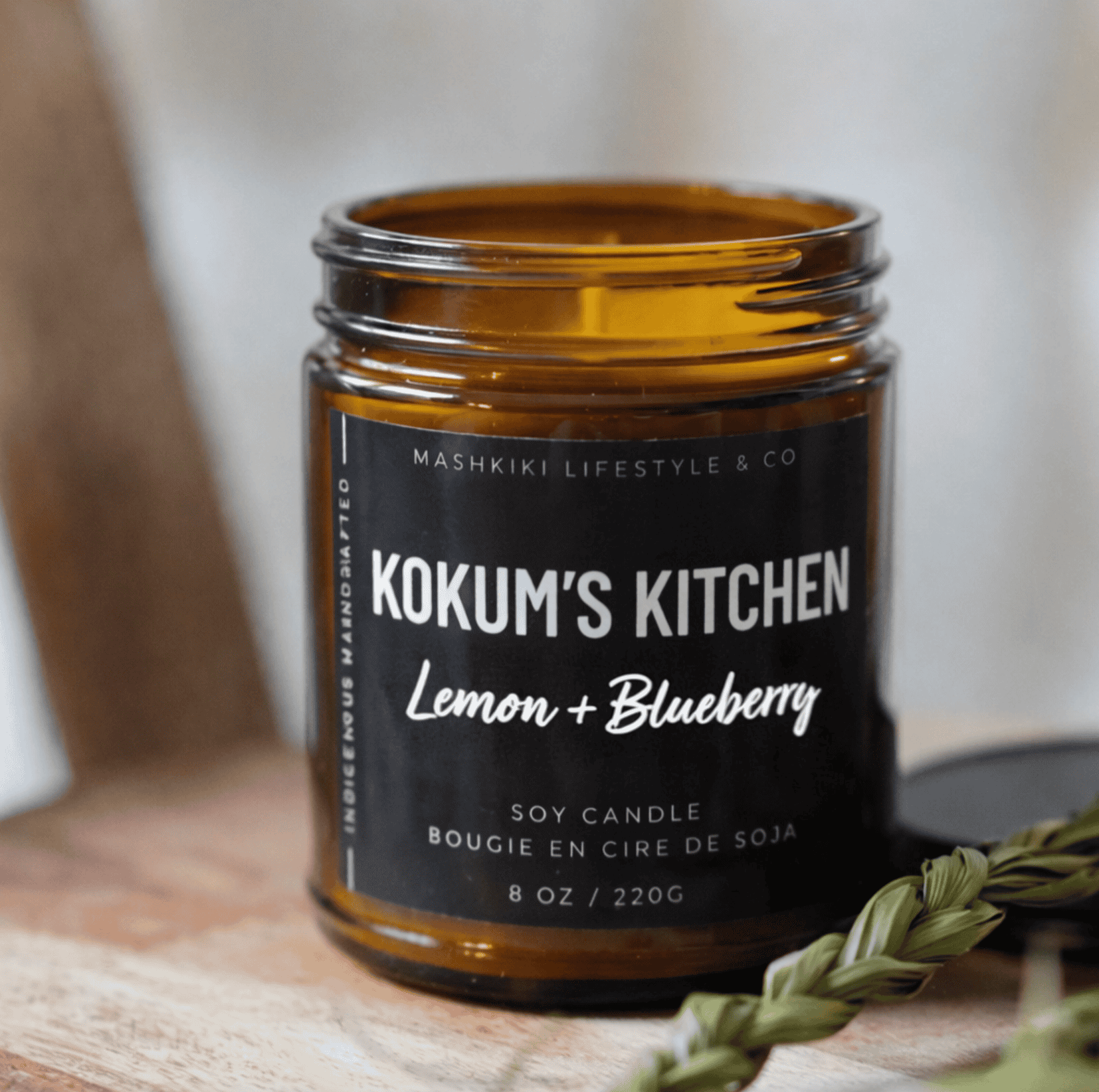 Mashkiki Kokum's Kitchen 8 oz amber glass soy candle, Lemon + Blueberry, beside a sweetgrass braid