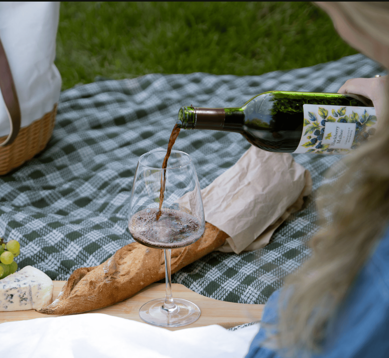 A glass of red wine being poured from a Cork It Blackberry Malbec bottle at a picnic