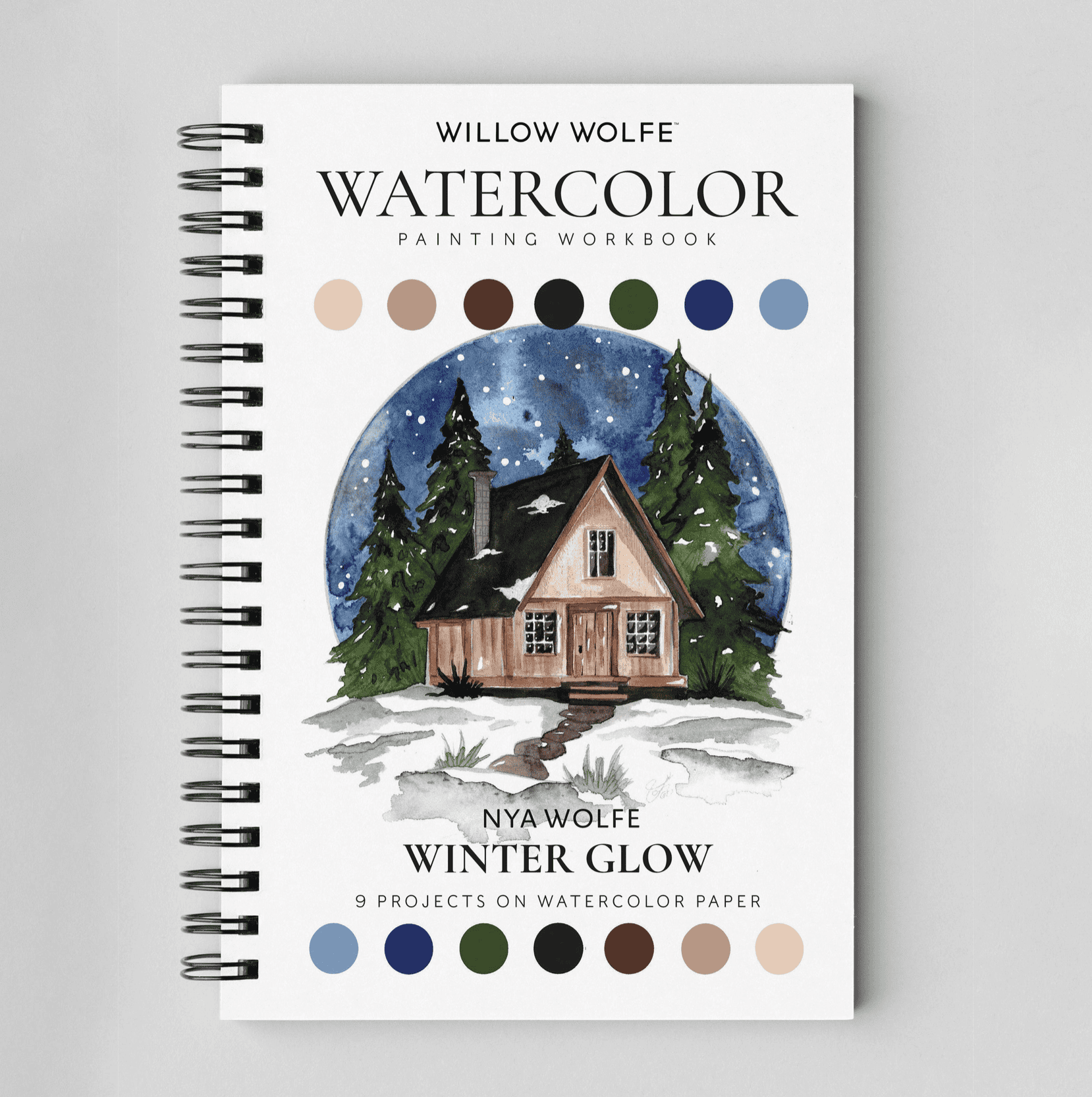 Winter Glow watercolour painting workbook by Nya Wolfe, front cover with a snowy cabin under a starry sky